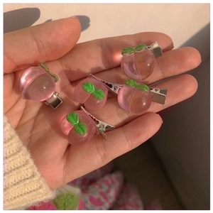 Detailed view of five pink resin peach hair clips held by hand against floral fabric