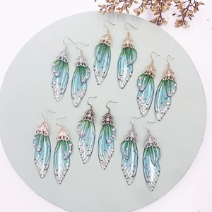 Macro detail of blue-green gradient butterfly wing earrings with sparkling rhinestones