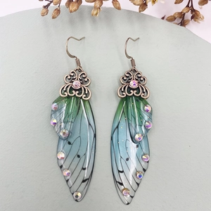 Detailed macro shot of translucent cicada wing earrings with green-blue gradient and rhinestones