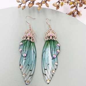 Detail of gradient blue and green cicada wing earrings with rhinestones on stone
