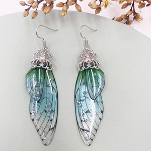 Macro view of gradient blue-green butterfly wing earrings on a soft green platform