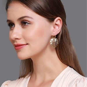 Boucles d'oreilles feuilles de monstera dorées portées avec un design tropical poli