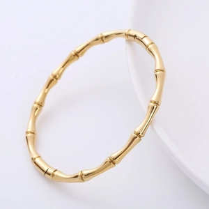 Polished gold bamboo-style stainless steel bangle resting on white ceramic plate