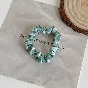 Detail of green camouflage silk hair scrunchie on marble background with wood decor