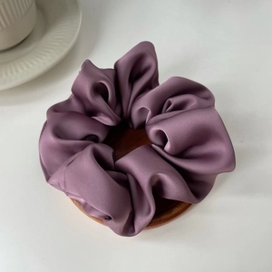 Detail of a large deep purple satin scrunchie with silk texture on a round wooden tray