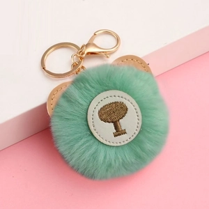 Detail of green faux fur pompom keychain with teddy bear ears and tree embroidery