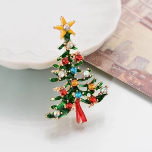 Close-up of green enamel Christmas tree brooch with colorful rhinestones on a ceramic dish