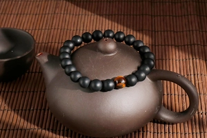 Detailed view of matte black agate beads and a tiger eye stone on a teapot lid