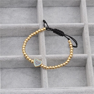 Detail of woven beaded bracelet with gold metal spheres and blue zircon heart charm