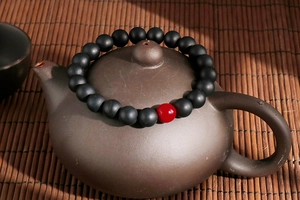 Detail of matte black agate beads and red accent bead on a zen ceramic teapot