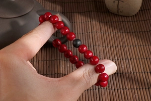 Detail of red beaded stretch bracelet with matte black stone on a peaceful tea-themed setting