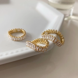 Detailed view of three gold baguette-cut zircon rings arranged on a white ceramic tray