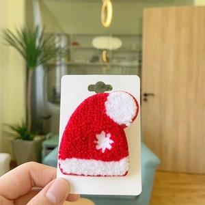 Detailed view of red plush Santa hat brooch with white snowflake pattern and pom-pom