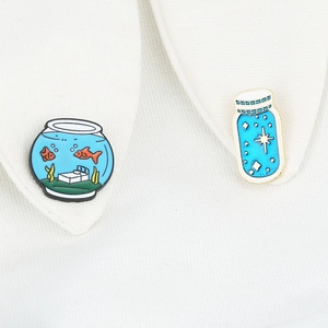 Cartoon goldfish bowl and blue star dream bottle enamel pins set on a white shirt collar
