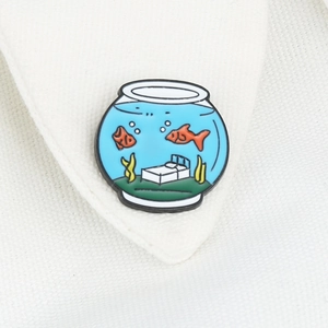 Macro detail of a fishbowl enamel pin showing goldfish and miniature furniture on a collar