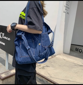 Detail of dark blue denim tote bag featuring dual front pockets and metal button closures