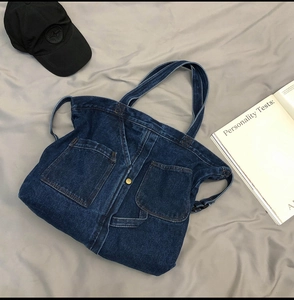 Flat lay of deep blue denim tote bag with large front pockets on a soft grey surface