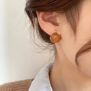 Close-up of caramel teardrop earrings with a glossy finish on a female model