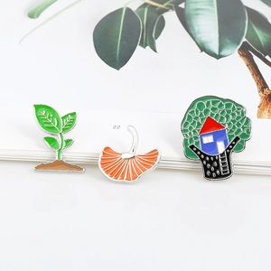 Enamel pins set featuring green seedling, ginkgo leaf, and tree on white paper