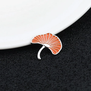 Macro view of an orange ginkgo leaf enamel brooch with silver metal trim on black texture