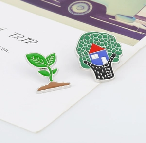 Detail of tree house and green seedling enamel pins on a white display background