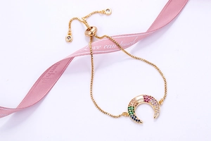 Detail van gouden armband met regenboog maanhanger op een elegant roze zijden lint