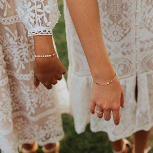 Close-up of golden adjustable disc chain bracelets on wrist with white lace dress