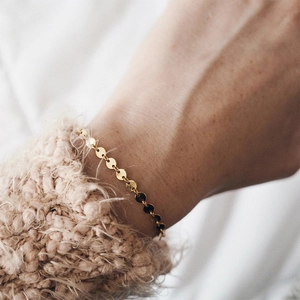 Detailed close-up of 14K gold-plated disc chain bracelet on wrist with knit sweater