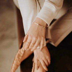 Detailed view of a gold disc chain bracelet paired with minimalist heart rings on a model