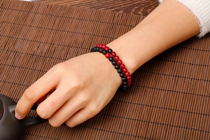 Detailed view of layered red and black 6mm beaded bracelets on a Zen style background