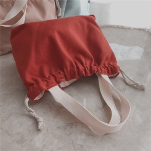 Detail view of a thick red canvas drawstring tote bag with off-white fabric handles