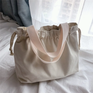 Detail of cream canvas handbag with drawstring closure and soft textured fabric handle