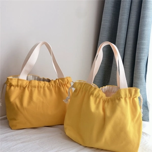 Detail of yellow canvas handbag featuring thick texture and white drawstring closure