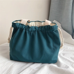 Detail of teal canvas handbag showing cream-colored drawstrings and woven handles