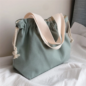 Detail of mint green canvas drawstring tote bag with off-white wide straps on bed
