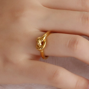 Polished 18K gold plated stainless steel knot ring shown on a model hand on white background
