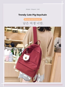 Close-up of a soft white plush pig keychain with golden chain on a red backpack