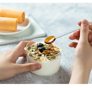 Primo piano di un cucchiaio in vetro resistente che versa miele in un dessert con bacche