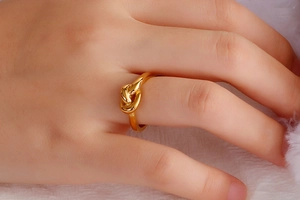 Detailed close-up of a polished gold knot ring worn on a finger against white velvet