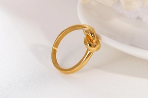 Close-up of golden knotted rope ring with minimalist polished metal finish on ceramic tray