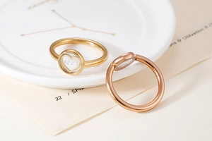 Detailed side view of gold and rose gold heart rings with clear stones on white dish