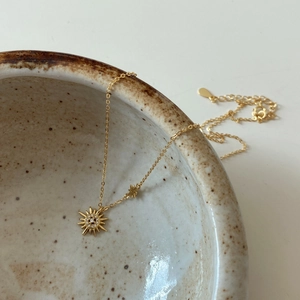 Macro detail of gold starburst necklace with zircons draped on a ceramic bowl