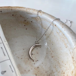Close-up of minimalist silver crescent moon pendant necklace on ceramic bowl edge