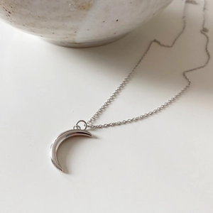 Close-up of a minimalist silver crescent moon pendant on a delicate cable chain