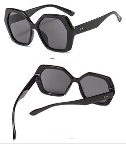 Detail view of black oversized polygonal sunglasses with golden rivets and grey lenses