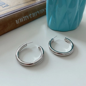 Detailed view of polished S925 sterling silver large C-shape hoop earrings on a blue vase
