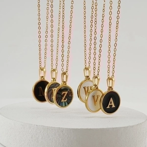 Detail of round gold pendant necklace with letter inlay and mother of pearl texture