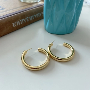 Detailed view of polished golden S925 silver large C-shaped hoop earrings on a desk