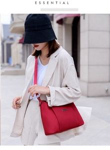 Detail of red nylon crossbody bag with adjustable strap and metal tag on a model