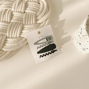 Set of 4 matte gray and black hair clips on a white display card with minimalist props